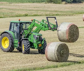 Tractor lifting hay bales in a field