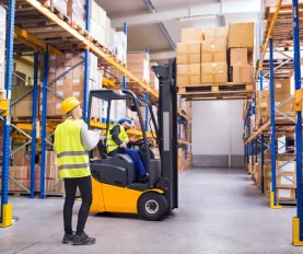 Workers operating forklift in warehouse.