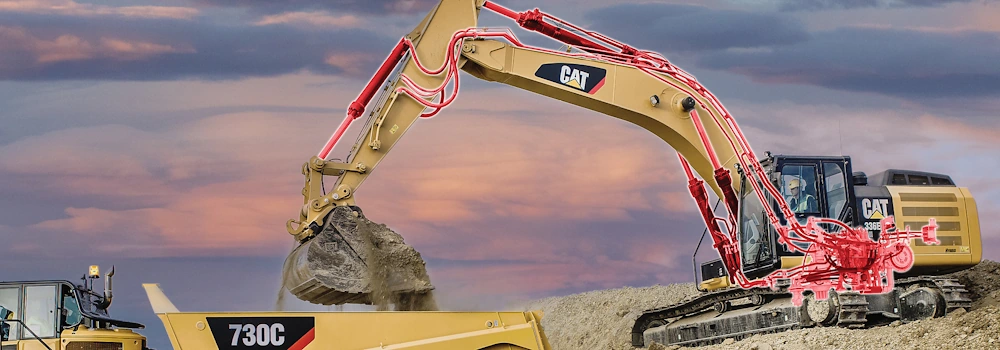 Excavator loading soil into dump truck at sunset.